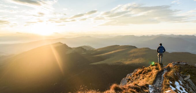 Man Standing on Mountain Looking at Sunset