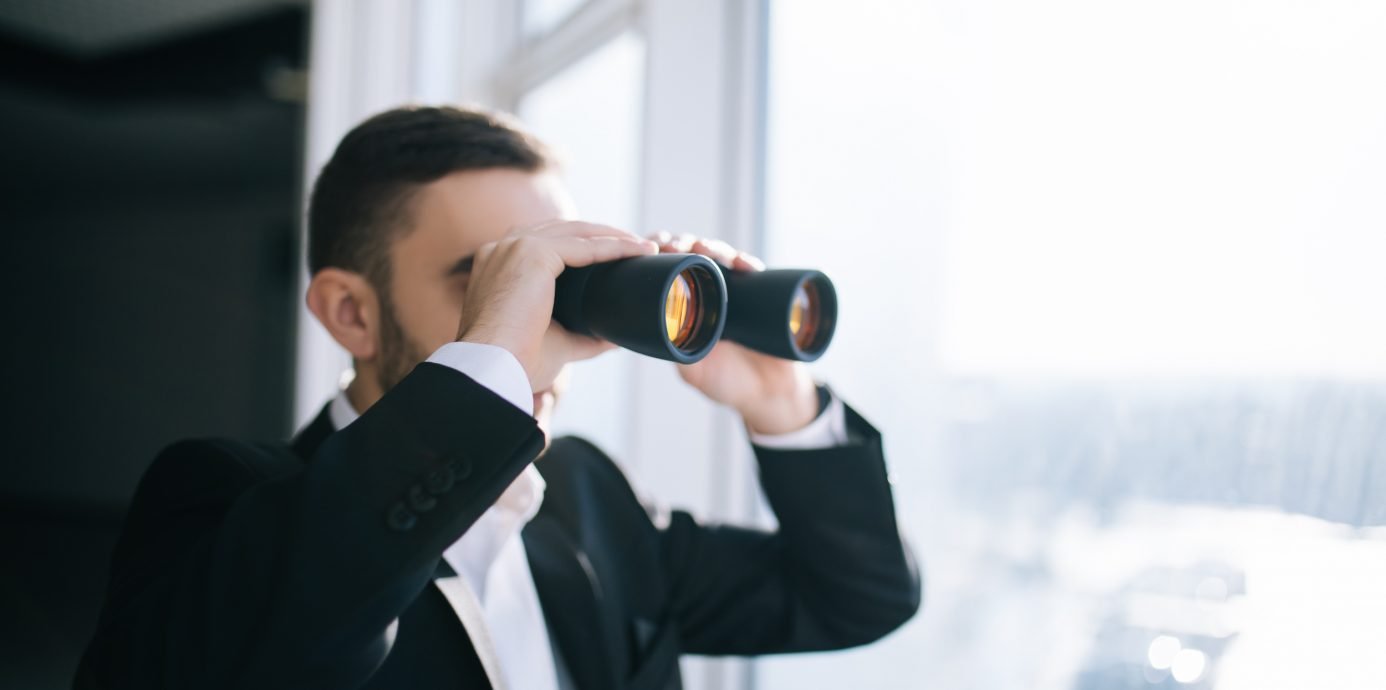 Man with binoculars looking out window